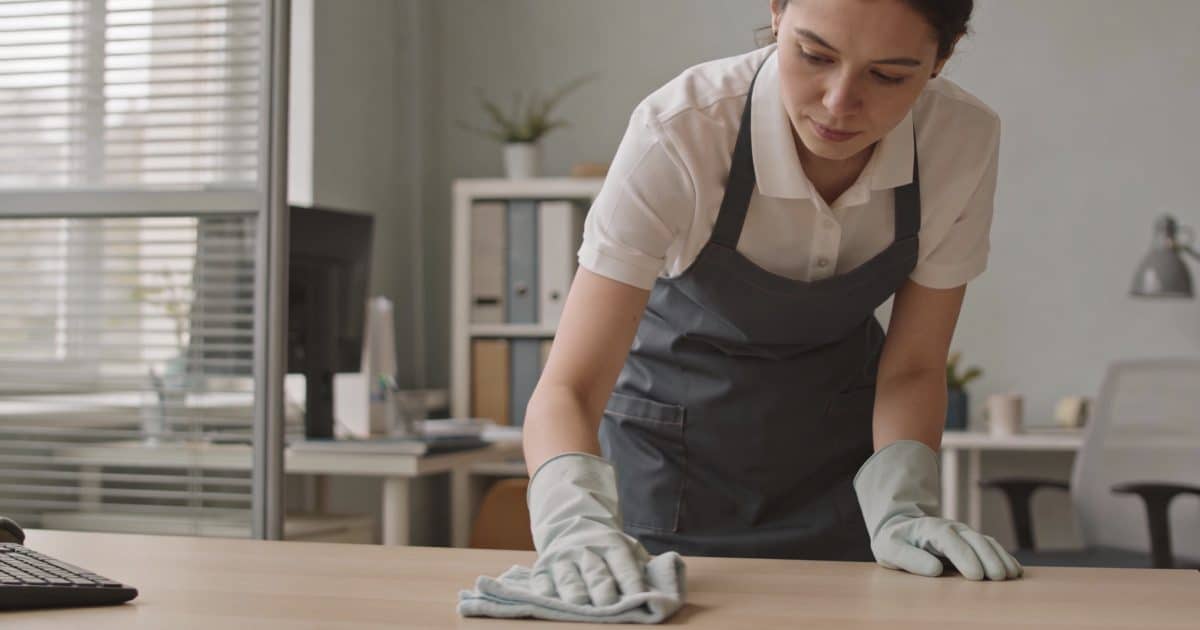 Femme en uniforme nettoyant un bureau avec chiffon