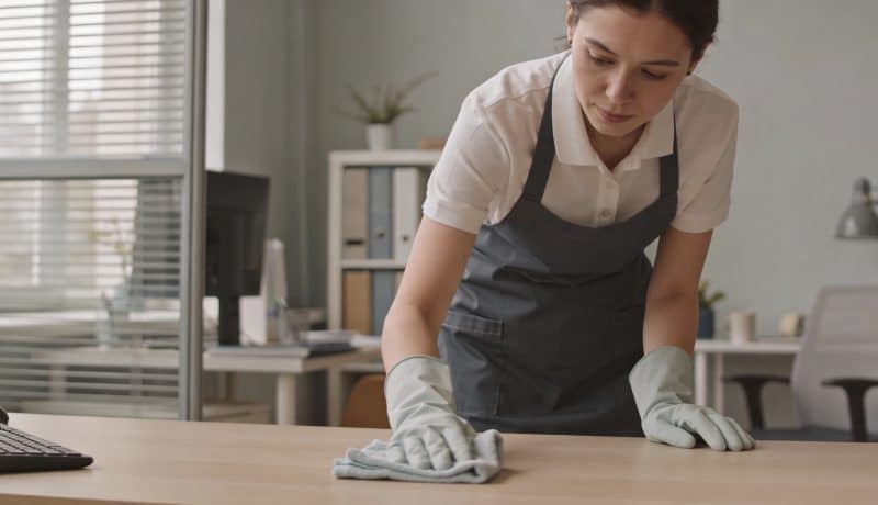 Femme en uniforme nettoyant un bureau avec chiffon