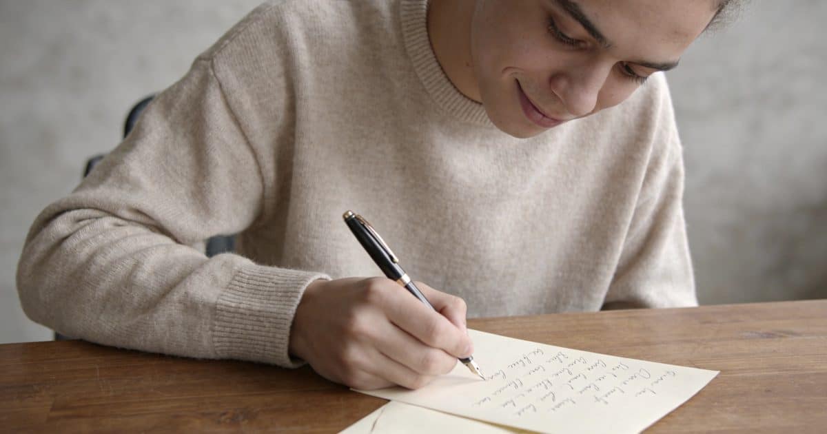 Jeune adulte souriant ecrit une lettre a la main