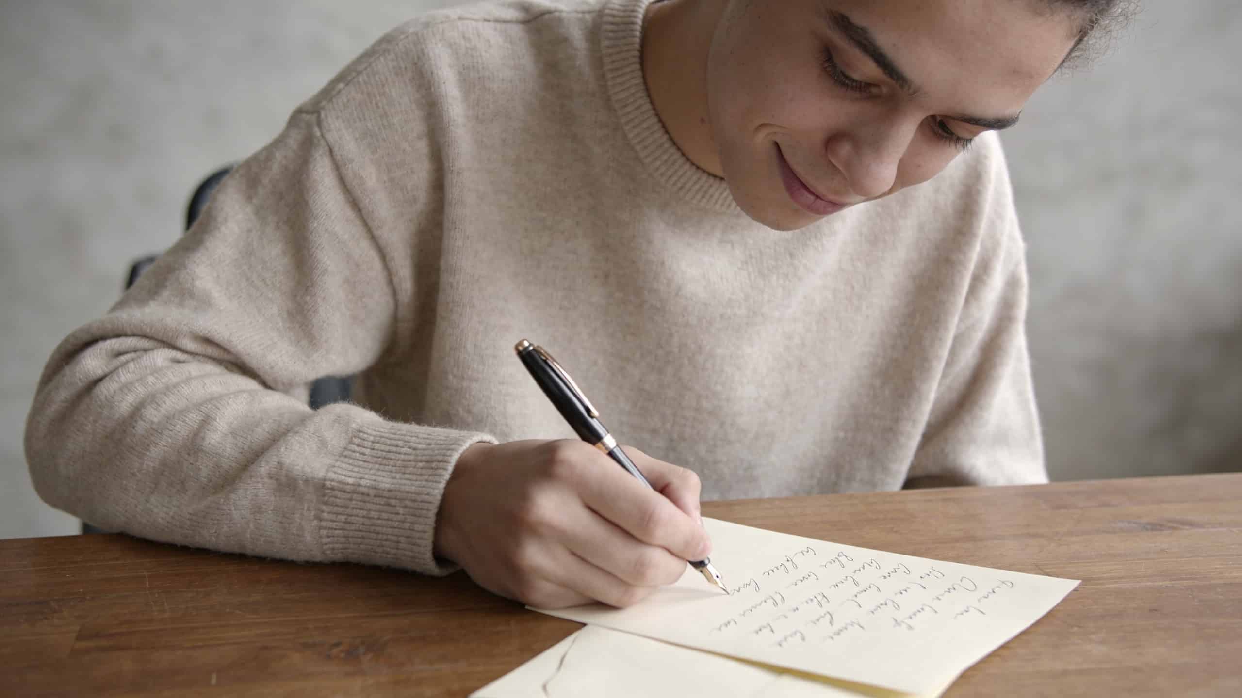 Jeune adulte souriant ecrit une lettre a la main