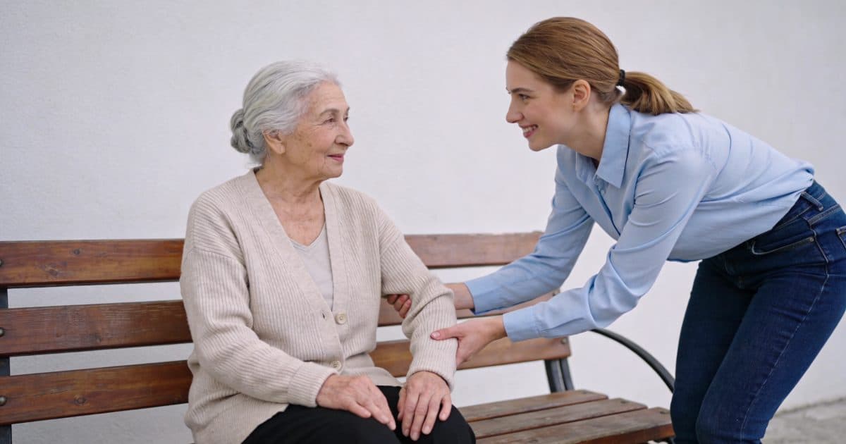 Jeune femme souriante aide une personne agee assise