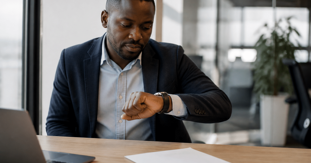 Employe assis au bureau regardant montre, contrat sur table