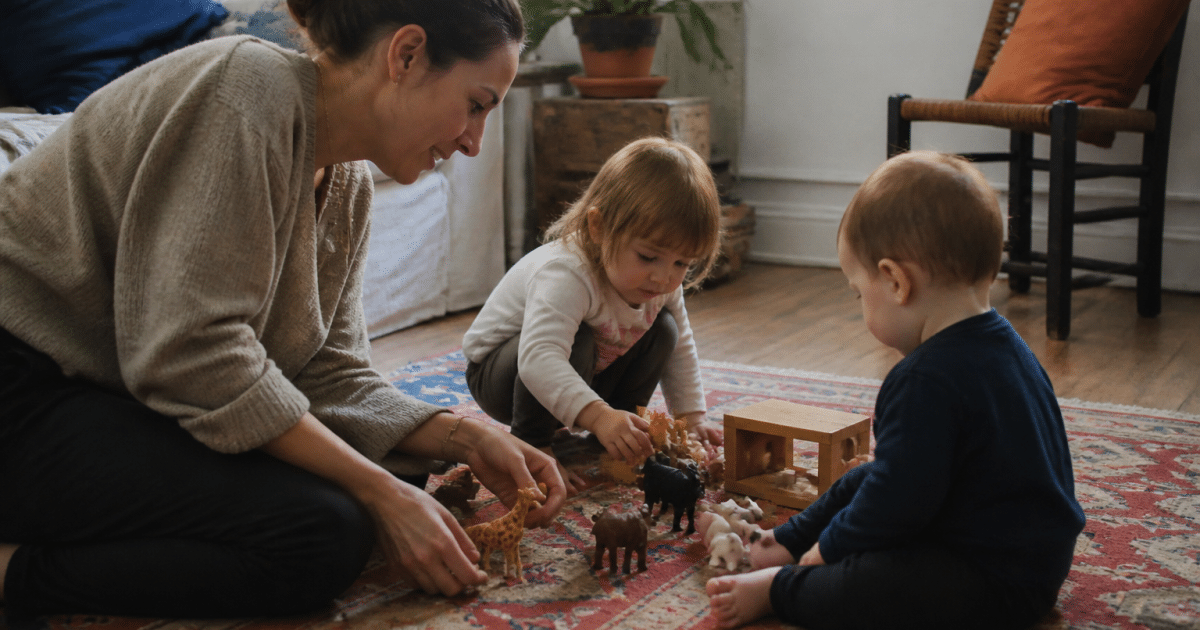 Femme assise jouant avec jeunes enfants sur tapis.