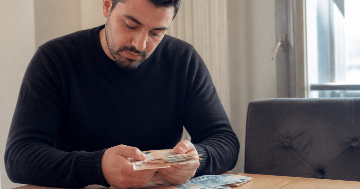 Homme assis comptant billets euros sur table.