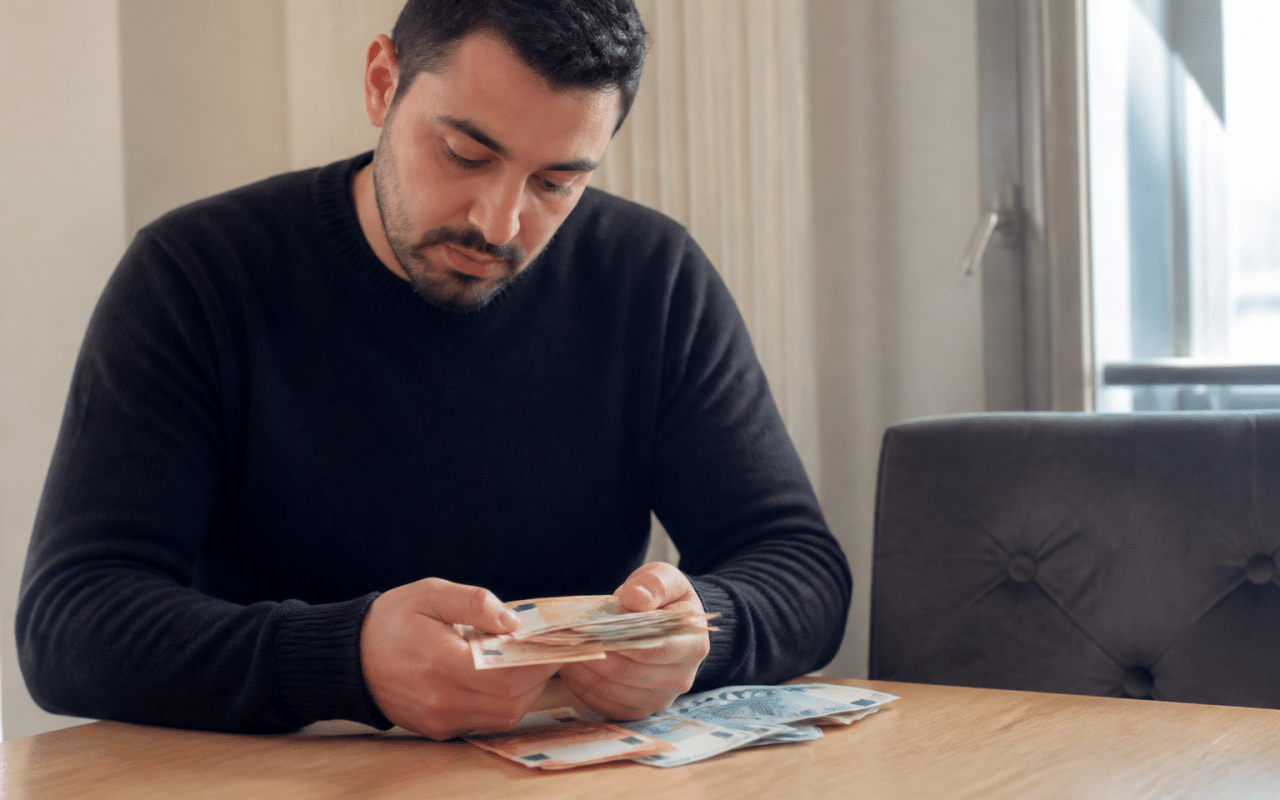 Homme assis comptant billets euros sur table.