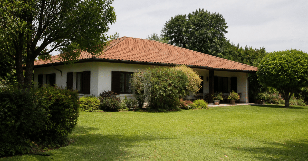 Maison basse entouree de jardins et pelouses vertes.