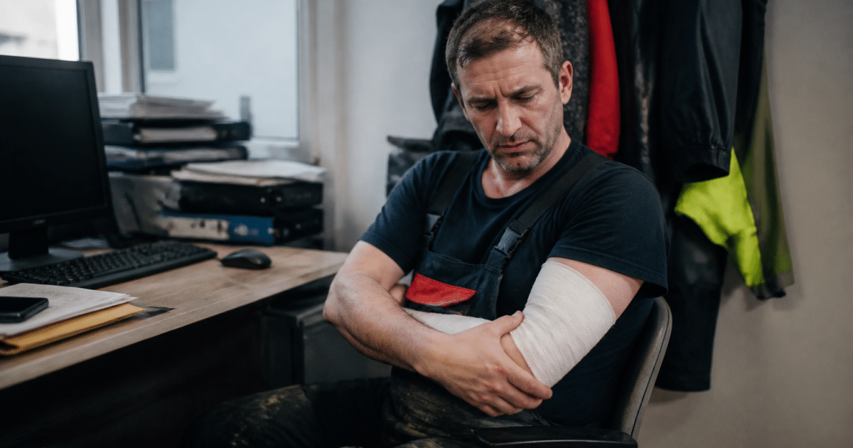 Ouvrier blesse assis tenant son bras immobile au bureau.