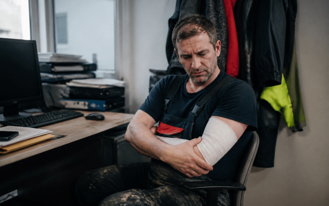 Ouvrier blesse assis tenant son bras immobile au bureau.