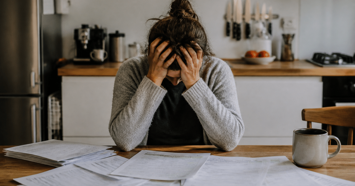 Personne assise, tête entre les mains, documents financiers éparpillés.
