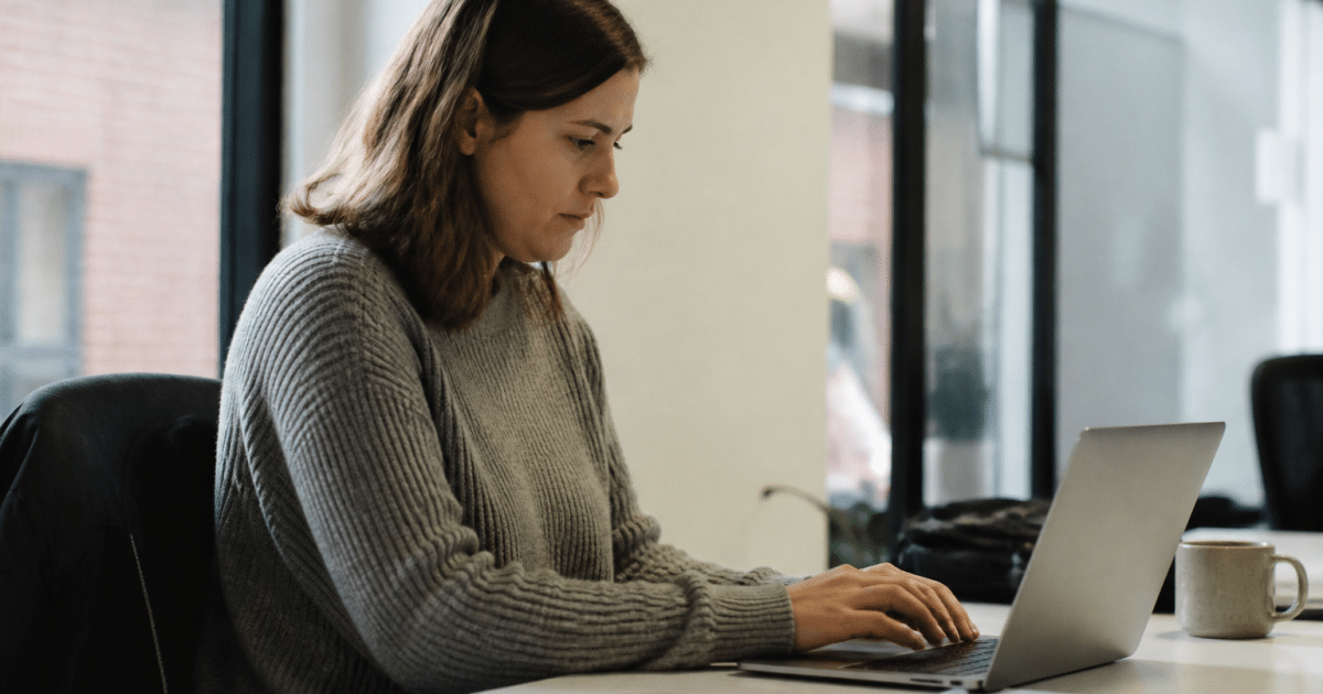 Personne assise au bureau travaillant sur ordinateur portable.