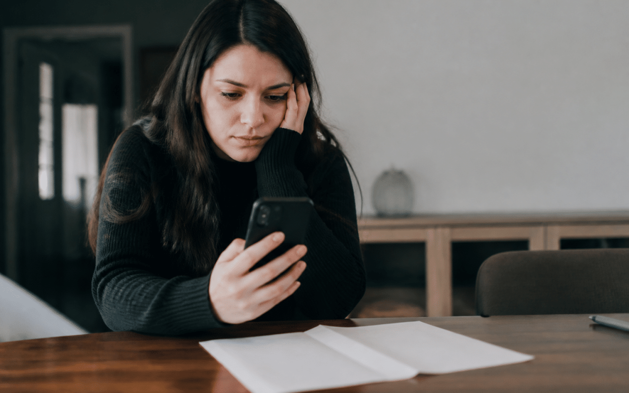 Personne consultant telephone avec relevé bancaire vide sur table