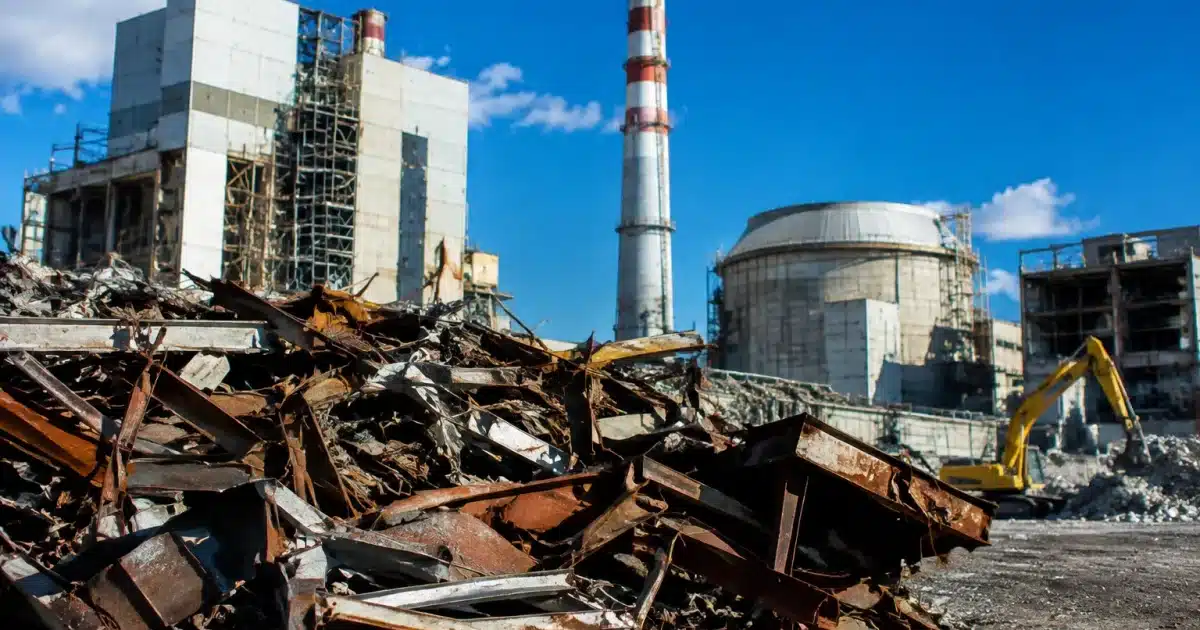 Debris stacked high beside industrial reactor buildings under deconstruction