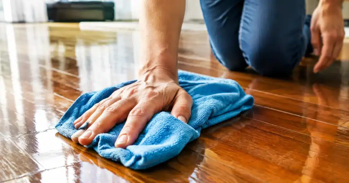 Mains tenant une serpilliere humide sur un parquet brillant en bois