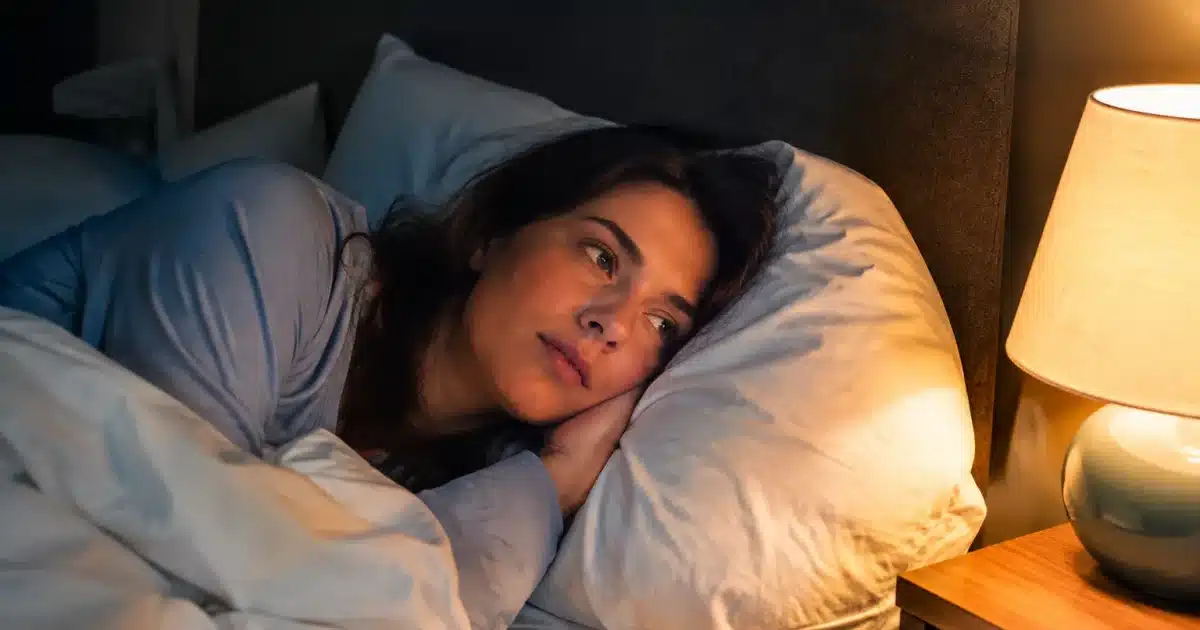 Personne allongee dans un lit avec lampe de chevet allumee la nuit