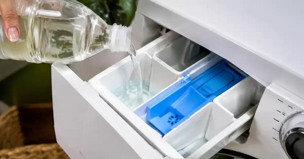 Bouteille de vinaigre blanc versée dans le compartiment d'adoucissant machine