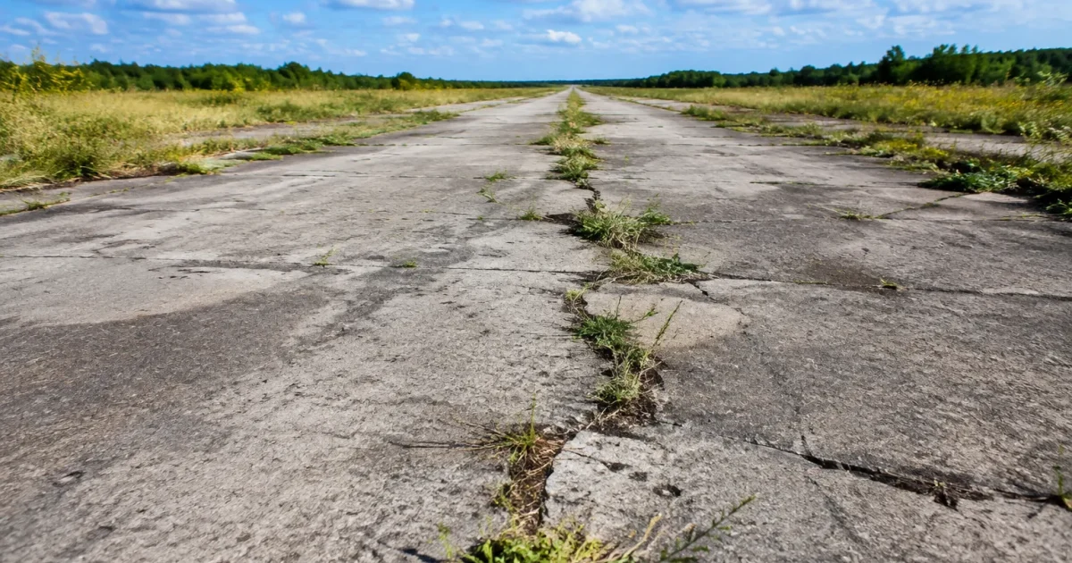 Longue piste beton grise fissures herbes invasives